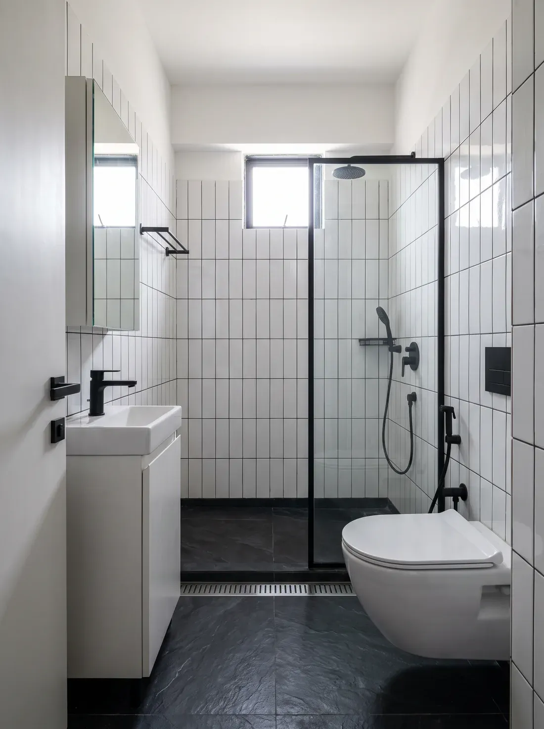 A narrow apartment bathroom with vertically stacked white tiles, a dark slate floor with a linear drain and black fittings — a design visualisation.